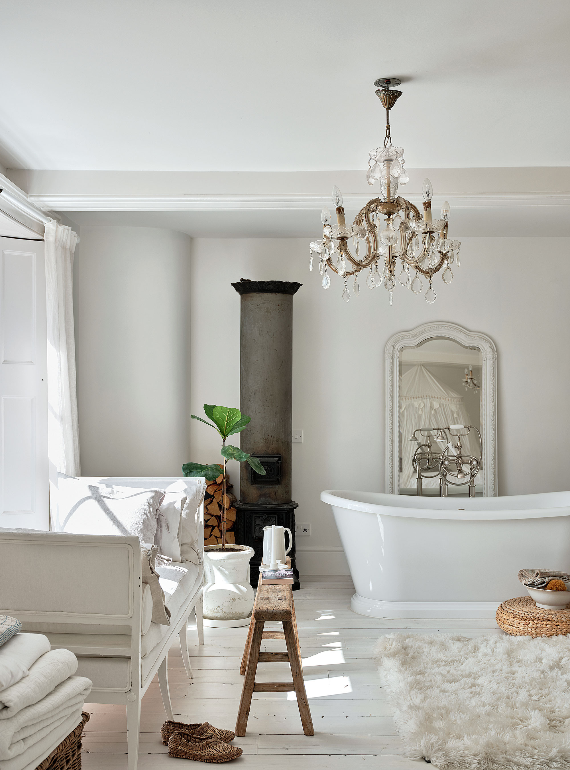 baño blanco con alfombra de piel de oveja, pisos de madera y paredes blancas con bañera independiente