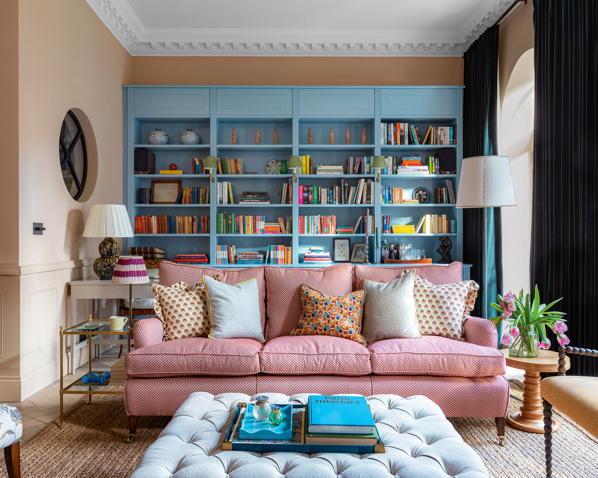Sala de estar colorida con estanterías azules hechas a medida, sofá rojo estampado, otomana, mesas auxiliares,