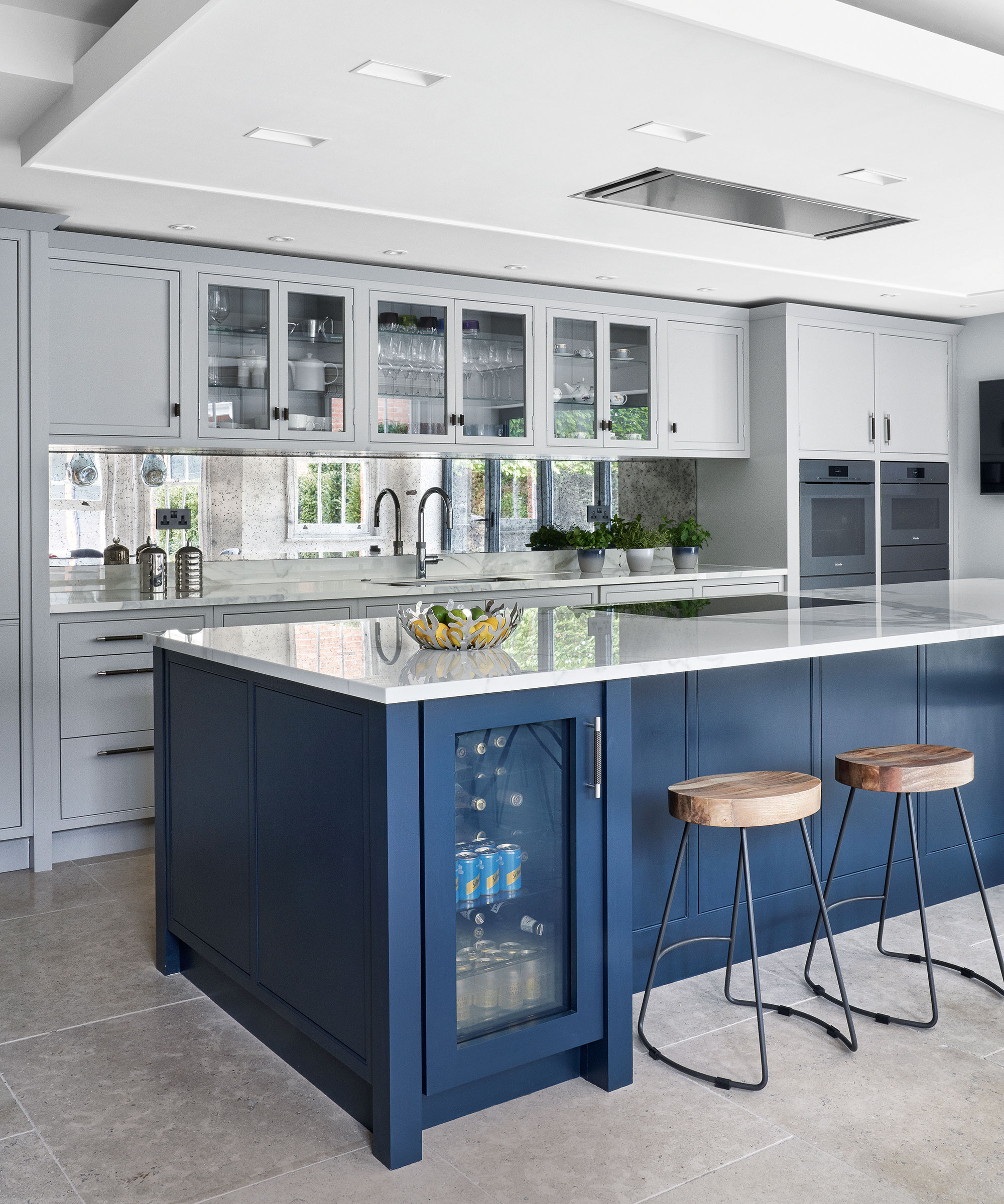 Cocina con pared de azulejos de espejo, paredes blancas y isla de cocina azul oscuro con taburetes de bar.