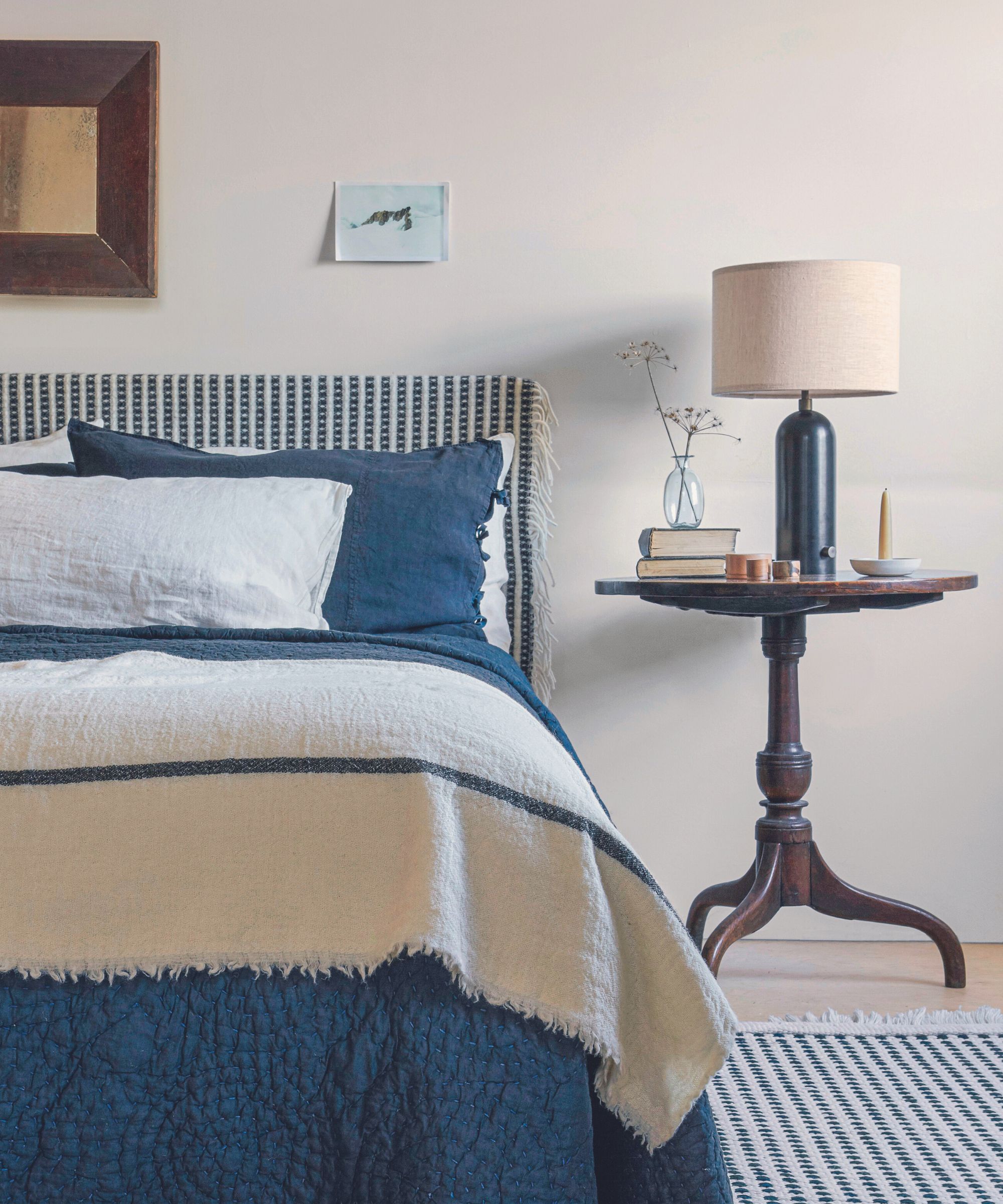 Cama doble con ropa de cama azul y crema contra una pared gris.