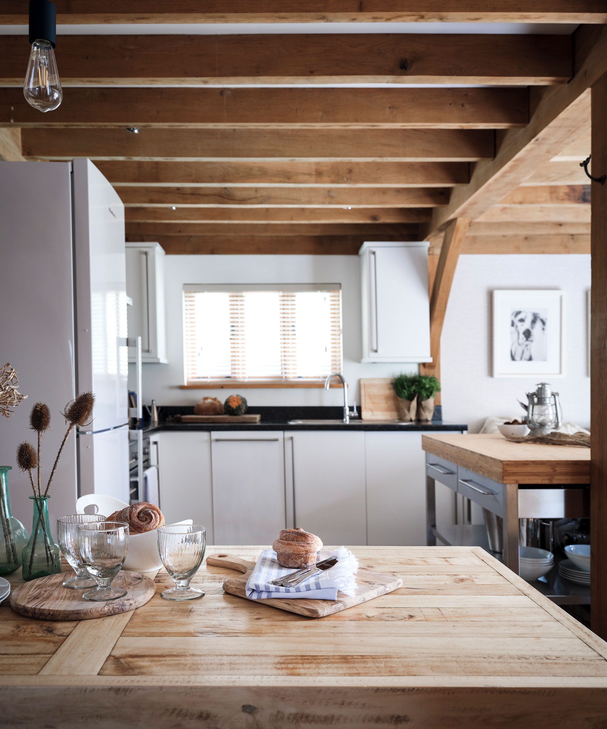 Pequeña cocina con vigas de madera, sobres, alacenas, ventana al fondo.