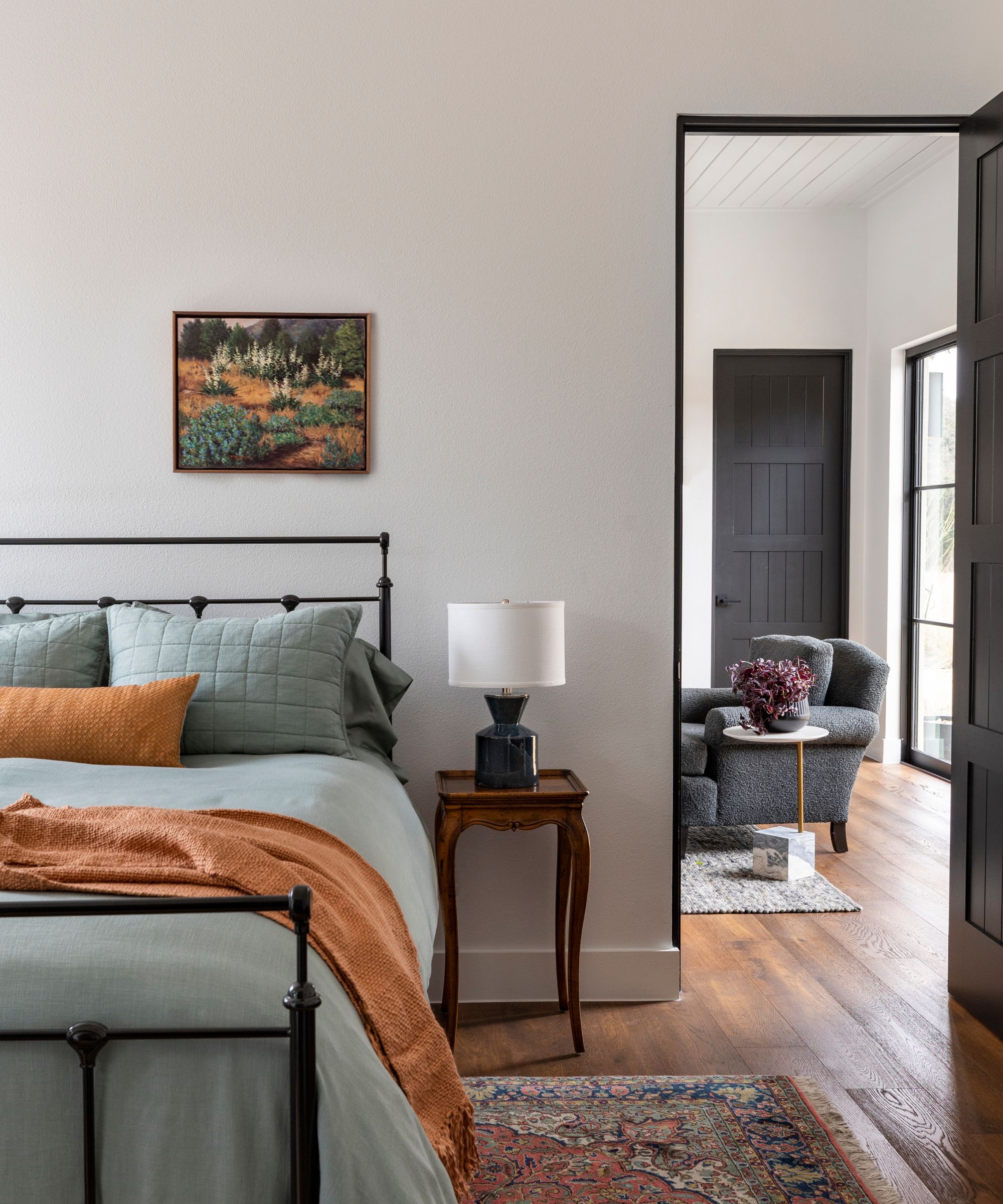 dormitorio con cama de hierro fundido con tiro de color óxido y vista a la sala de estar con paredes blancas