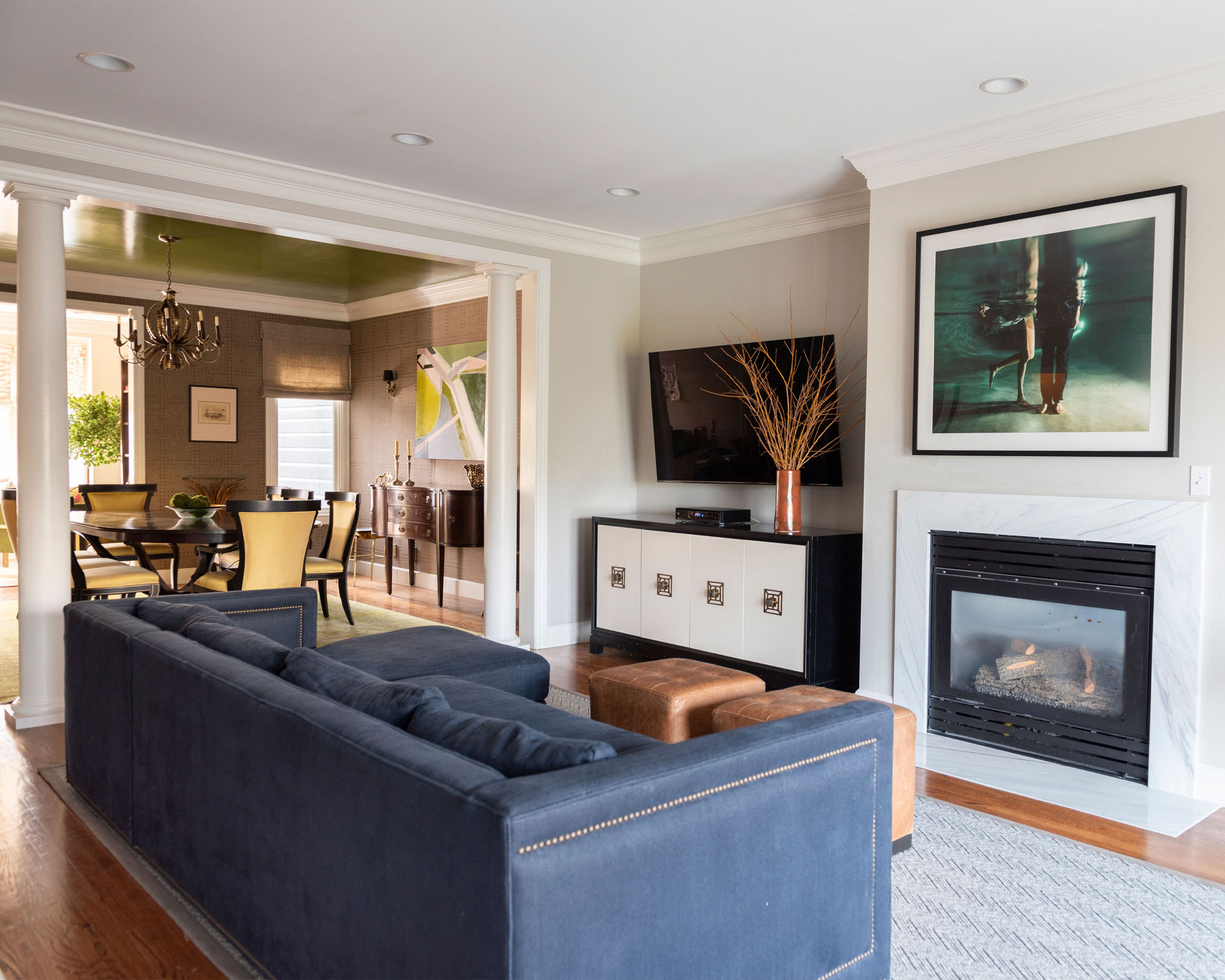 Moderna sala de estar y comedor de planta abierta, TV en la pared, aparador, chimenea, sofá azul, dos pufs de cuero