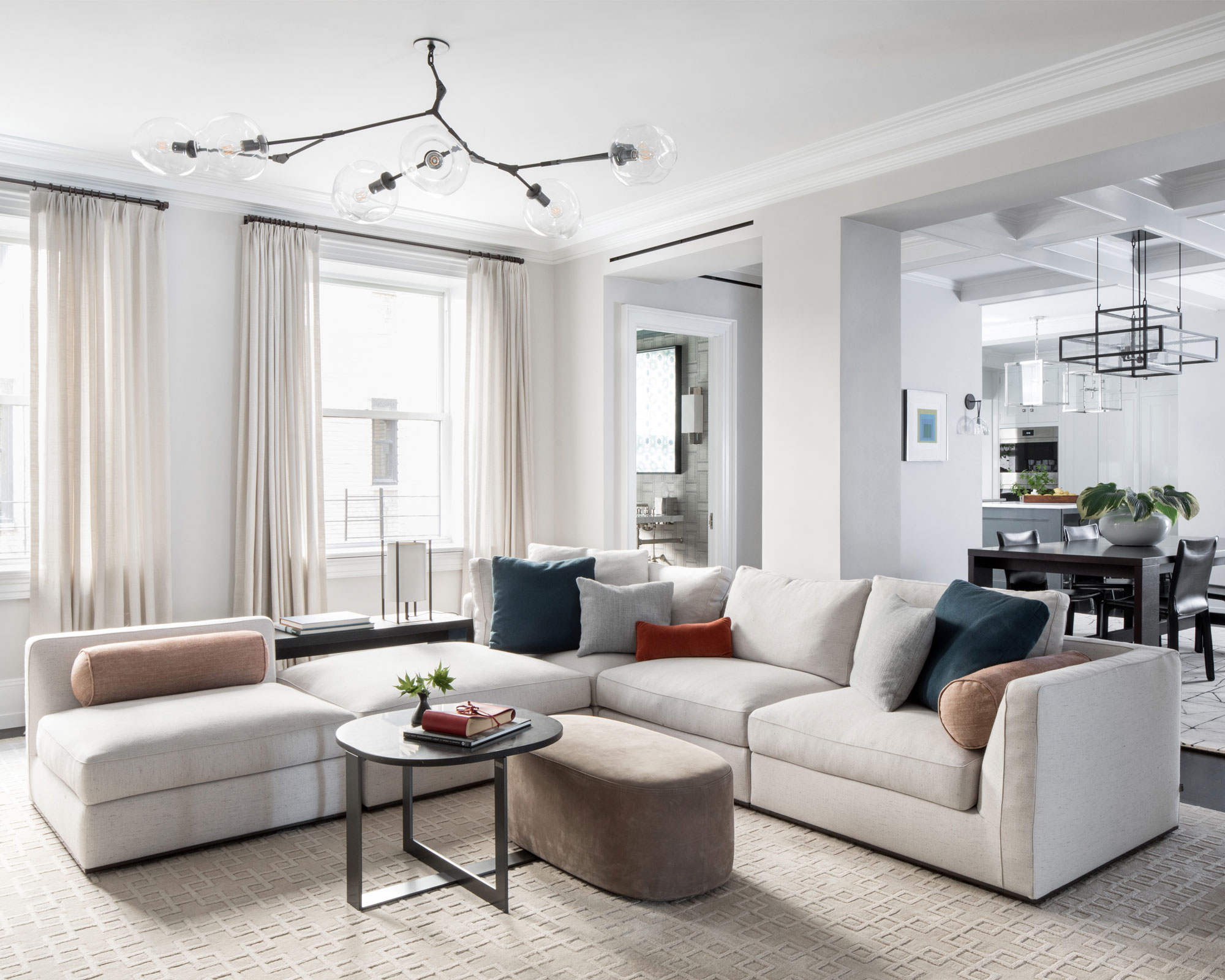 Moderna sala de estar blanca con sofá color crema, nido de mesas, lámpara de techo escultórica, cocina al fondo